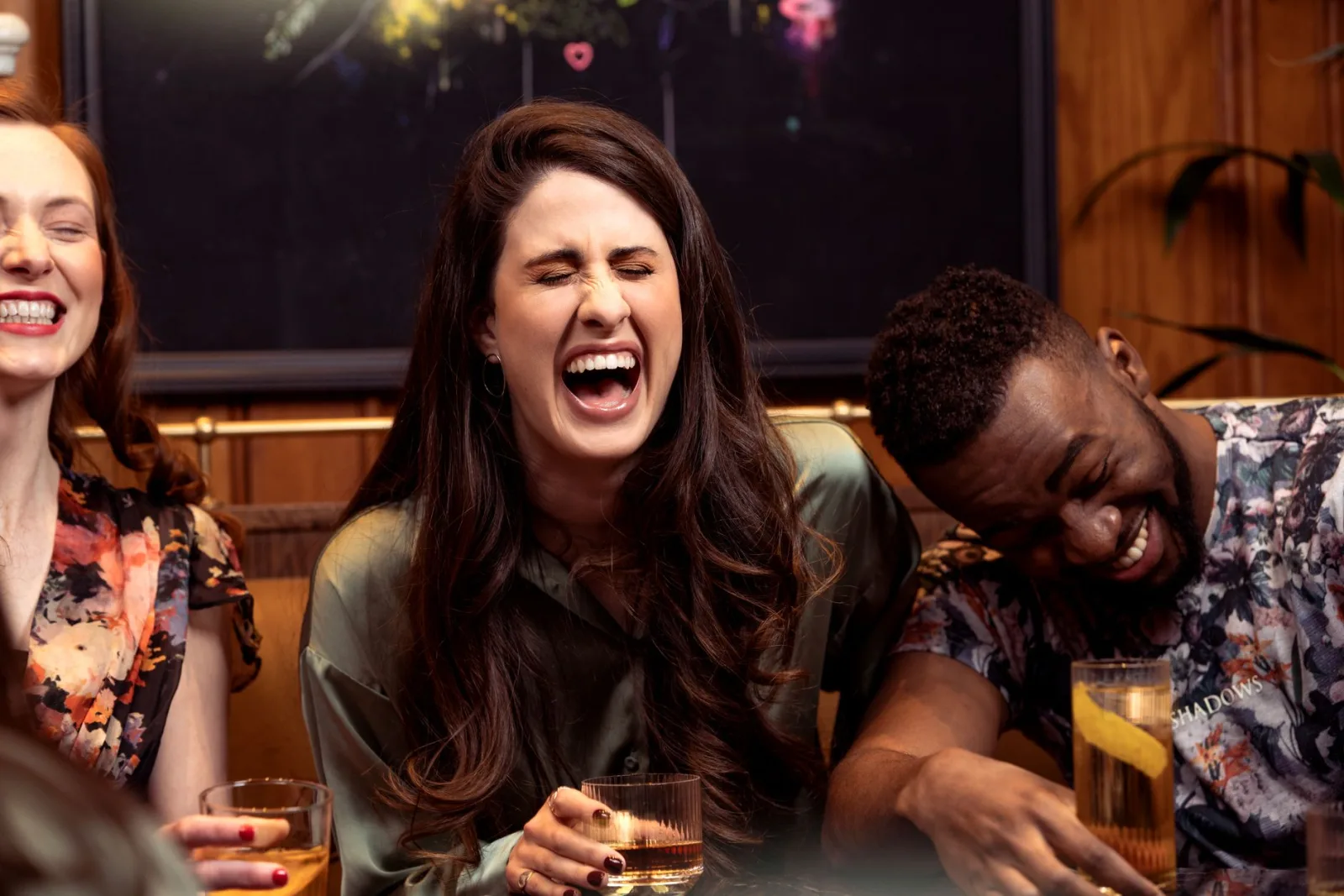 Groupe d'amis qui rient autour de cocktails dans un bar